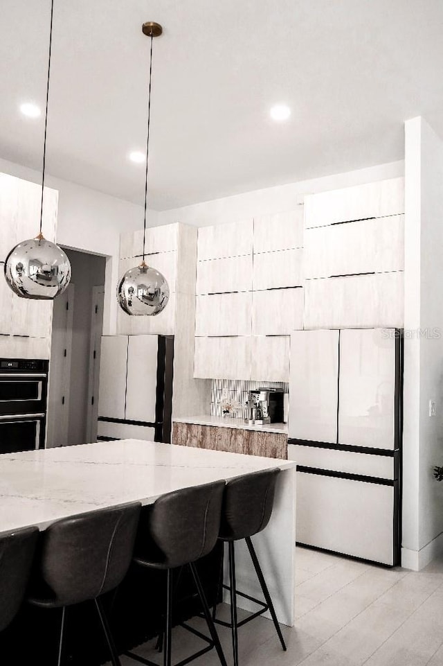 kitchen with a breakfast bar, decorative light fixtures, modern cabinets, dobule oven black, and light stone countertops