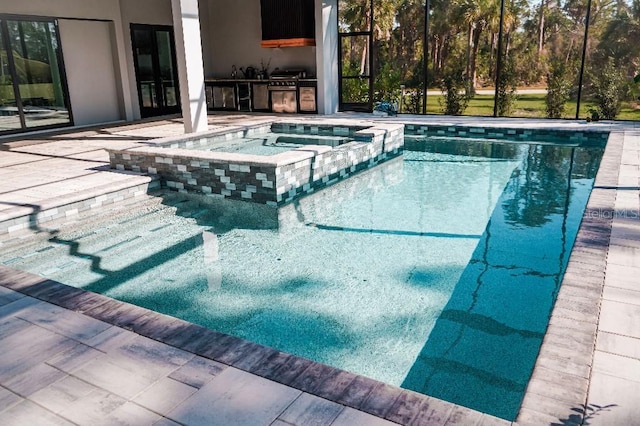 view of swimming pool featuring a pool with connected hot tub, an outdoor kitchen, and a patio