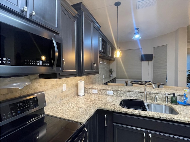 kitchen featuring sink, tasteful backsplash, light stone counters, stove, and decorative light fixtures