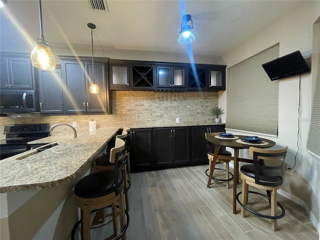 kitchen featuring pendant lighting, black electric range, light hardwood / wood-style flooring, light stone countertops, and tasteful backsplash