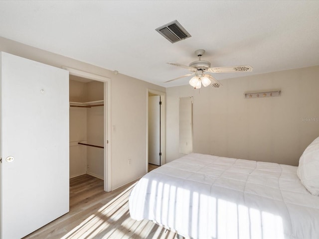 bedroom with a walk in closet, a closet, ceiling fan, and light hardwood / wood-style floors