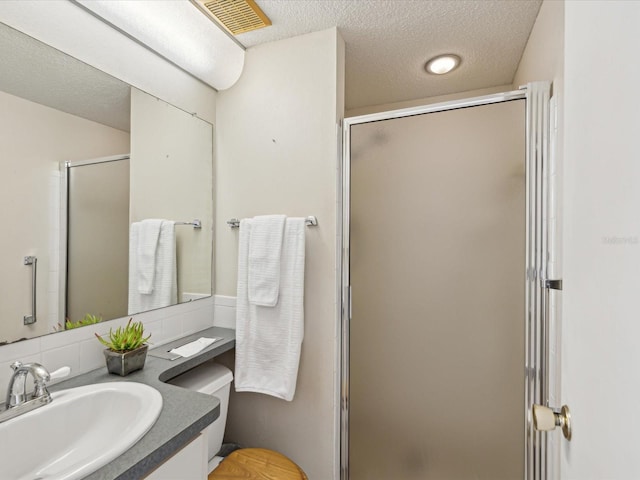 bathroom with vanity, toilet, a shower with shower door, and a textured ceiling