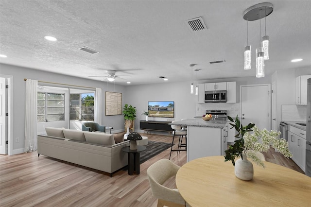 living room featuring ceiling fan, light hardwood / wood-style flooring, and a textured ceiling