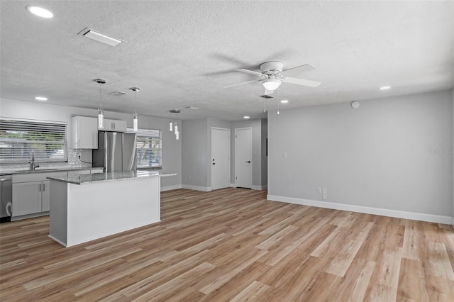 kitchen featuring light stone counters, stainless steel appliances, pendant lighting, white cabinets, and a kitchen island