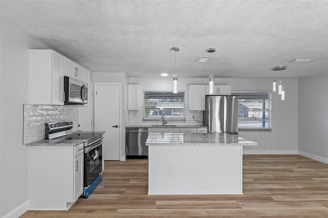 kitchen with white cabinets, decorative light fixtures, stainless steel appliances, and a kitchen island