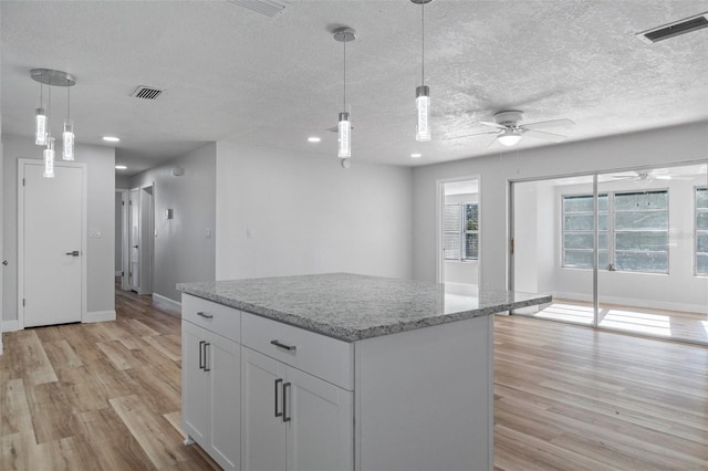 kitchen with light stone counters, a textured ceiling, decorative light fixtures, white cabinets, and light wood-type flooring