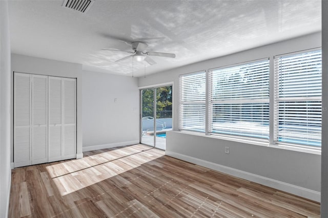 unfurnished bedroom featuring access to exterior, a textured ceiling, ceiling fan, light hardwood / wood-style floors, and a closet