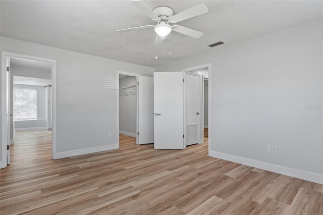 unfurnished bedroom with light hardwood / wood-style flooring, ceiling fan, a spacious closet, a textured ceiling, and a closet