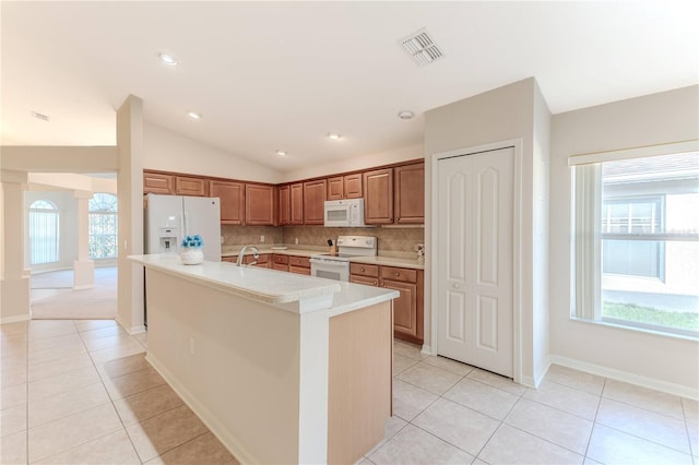 kitchen featuring tasteful backsplash, vaulted ceiling, white appliances, a center island with sink, and light tile patterned floors