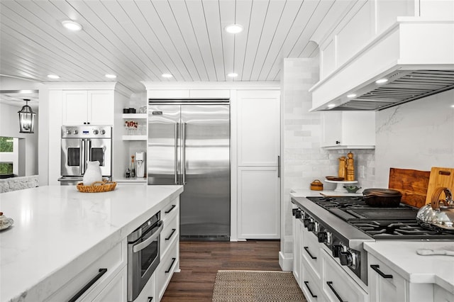 kitchen with white cabinets, dark hardwood / wood-style floors, light stone countertops, appliances with stainless steel finishes, and custom range hood