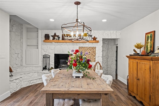 dining area featuring dark hardwood / wood-style flooring, built in features, a fireplace, and an inviting chandelier