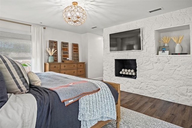 bedroom with hardwood / wood-style floors, a stone fireplace, and a notable chandelier