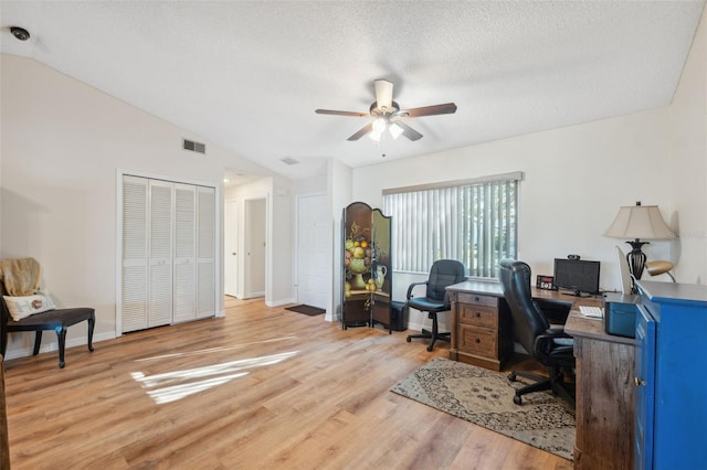 office area with a textured ceiling, a ceiling fan, vaulted ceiling, visible vents, and light wood finished floors