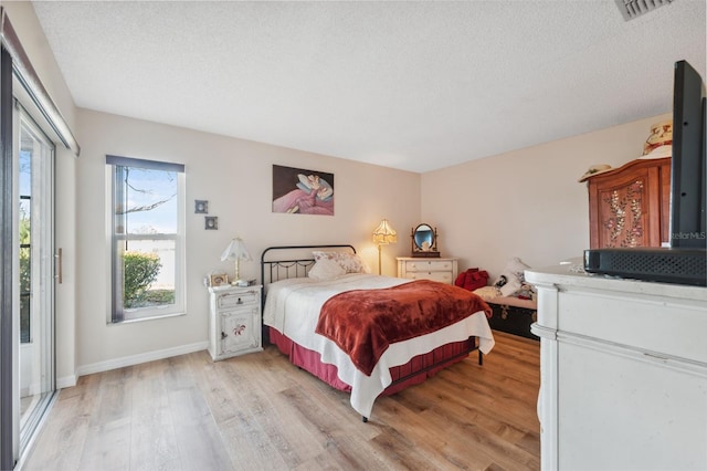 bedroom featuring visible vents, baseboards, light wood finished floors, and a textured ceiling