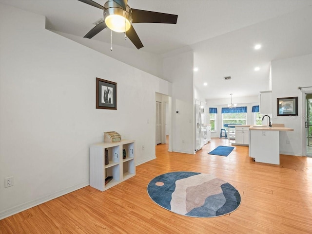 living room featuring ceiling fan with notable chandelier, light hardwood / wood-style flooring, and sink