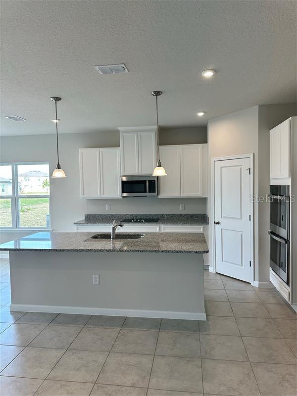 kitchen with a center island with sink, appliances with stainless steel finishes, pendant lighting, and white cabinets