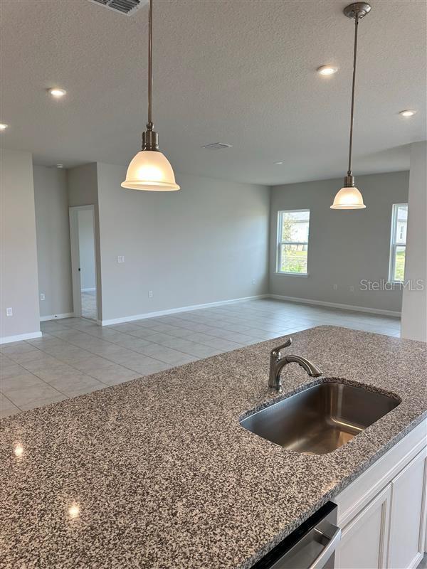 kitchen featuring light tile patterned floors, hanging light fixtures, a textured ceiling, white cabinets, and sink