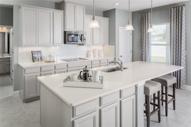 kitchen featuring tasteful backsplash, sink, an island with sink, and black electric stovetop