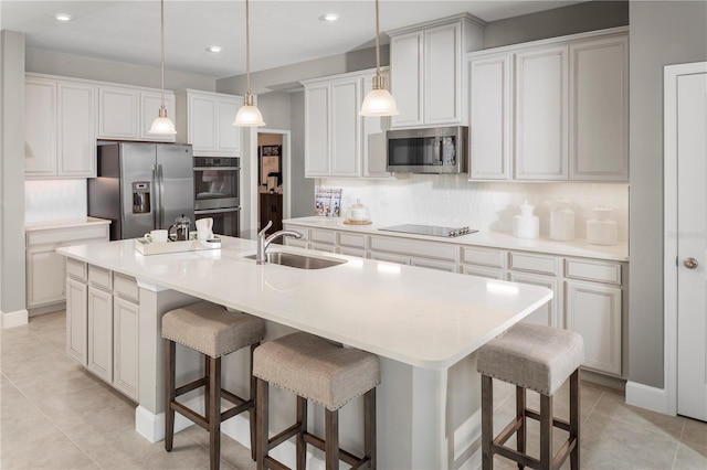 kitchen featuring stainless steel appliances, a kitchen island with sink, sink, white cabinets, and a breakfast bar area