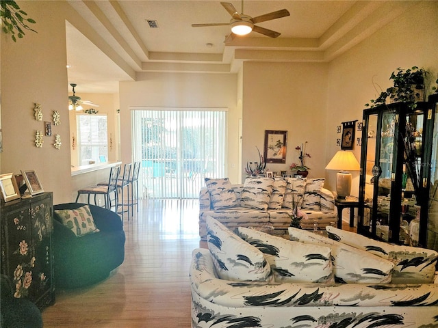 living room with wood-type flooring, a tray ceiling, and ceiling fan