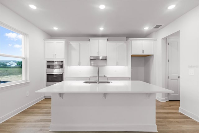 kitchen with double oven, a center island with sink, and white cabinets