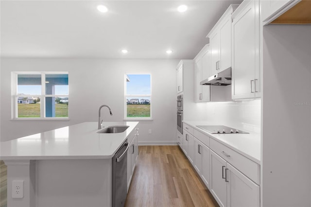 kitchen with sink, black electric cooktop, white cabinetry, and an island with sink