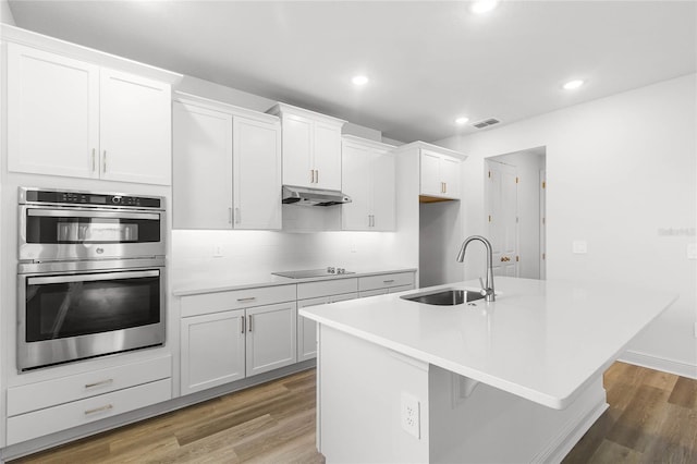 kitchen with white cabinets, stainless steel double oven, a center island with sink, and sink