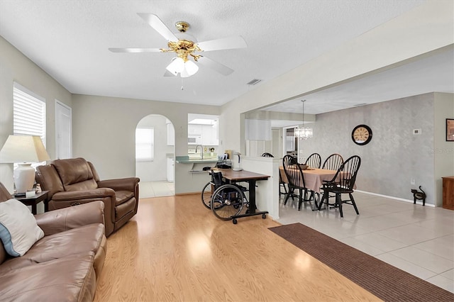 living room featuring ceiling fan with notable chandelier, a textured ceiling, light wood-type flooring, and sink