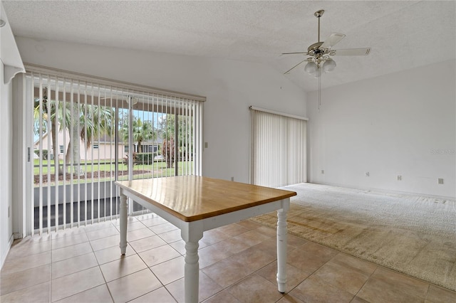 unfurnished dining area with lofted ceiling, light tile patterned floors, a ceiling fan, and light colored carpet