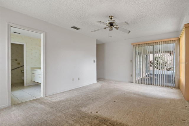 empty room featuring ceiling fan, visible vents, a textured ceiling, and light colored carpet