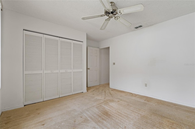 unfurnished bedroom featuring baseboards, visible vents, light colored carpet, a textured ceiling, and a closet