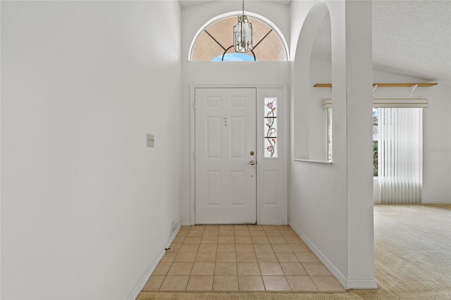 foyer entrance with a chandelier, light tile patterned floors, a textured ceiling, light colored carpet, and baseboards