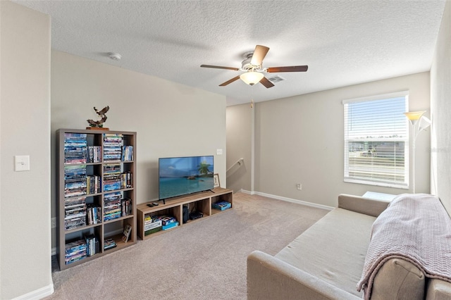 living room featuring ceiling fan, light colored carpet, and a textured ceiling