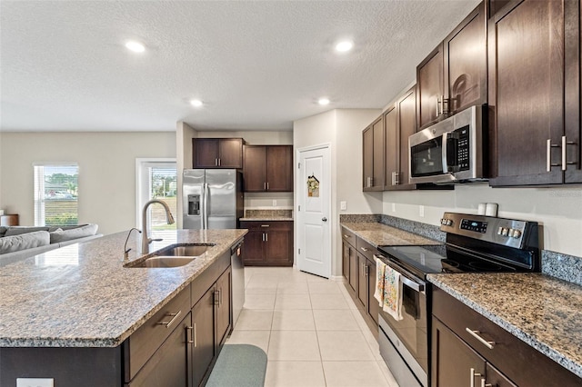 kitchen featuring light stone countertops, sink, stainless steel appliances, a center island with sink, and light tile patterned flooring