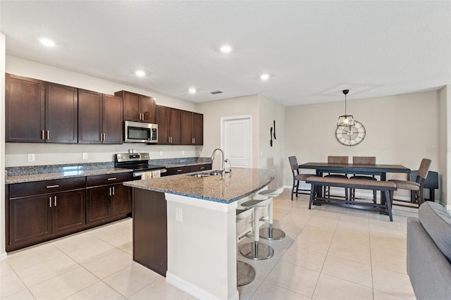 kitchen with sink, hanging light fixtures, stainless steel appliances, a kitchen breakfast bar, and a center island with sink