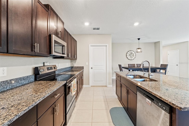 kitchen with sink, light stone countertops, light tile patterned floors, appliances with stainless steel finishes, and decorative light fixtures