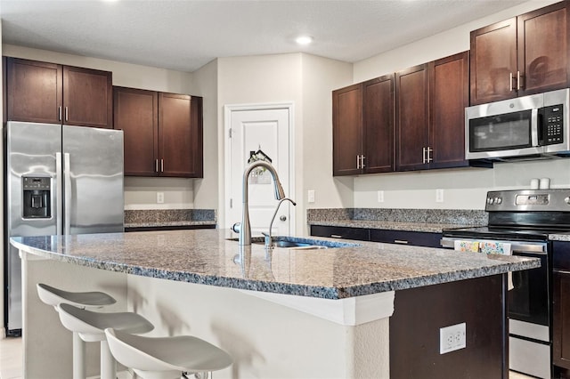 kitchen with a kitchen bar, a kitchen island with sink, sink, and stainless steel appliances