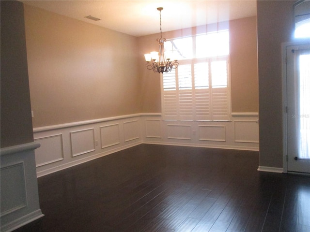 unfurnished room with plenty of natural light, dark hardwood / wood-style flooring, and a chandelier