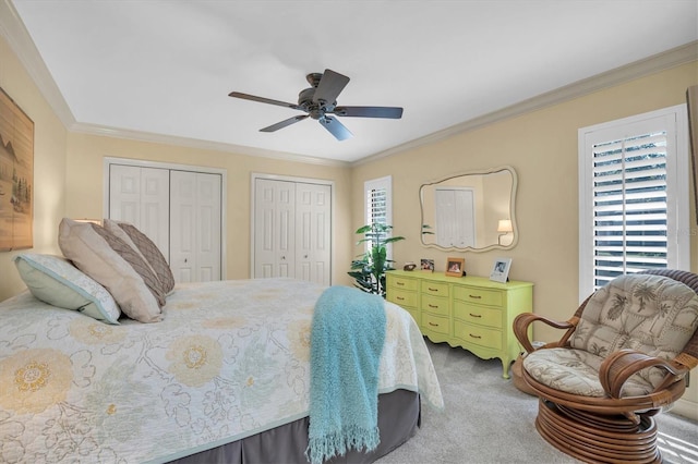 carpeted bedroom featuring ceiling fan, ornamental molding, and two closets