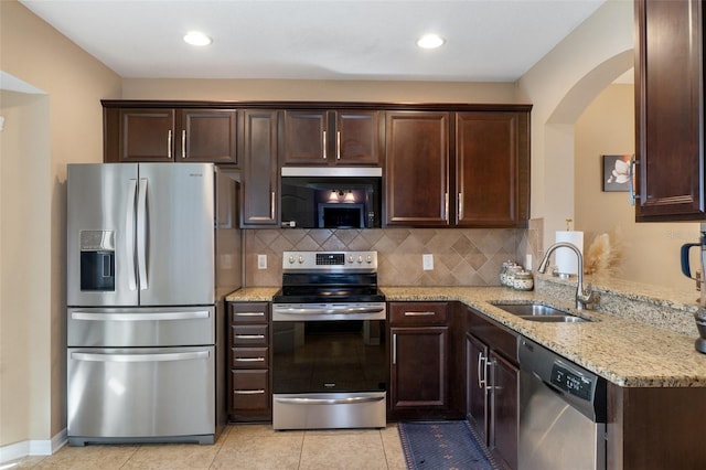 kitchen with light stone counters, dark brown cabinetry, a sink, appliances with stainless steel finishes, and decorative backsplash