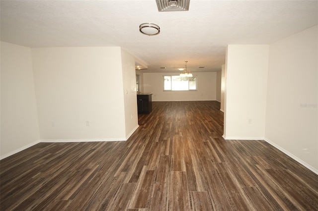 empty room with dark hardwood / wood-style flooring and an inviting chandelier