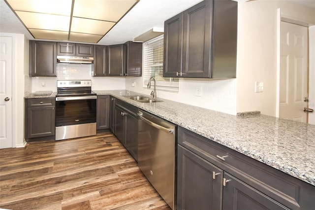 kitchen with appliances with stainless steel finishes, light stone counters, dark brown cabinets, sink, and dark hardwood / wood-style floors