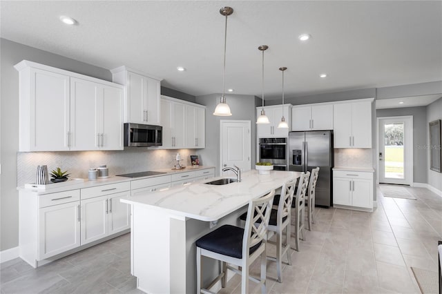 kitchen with a breakfast bar, stainless steel appliances, sink, a center island with sink, and white cabinetry