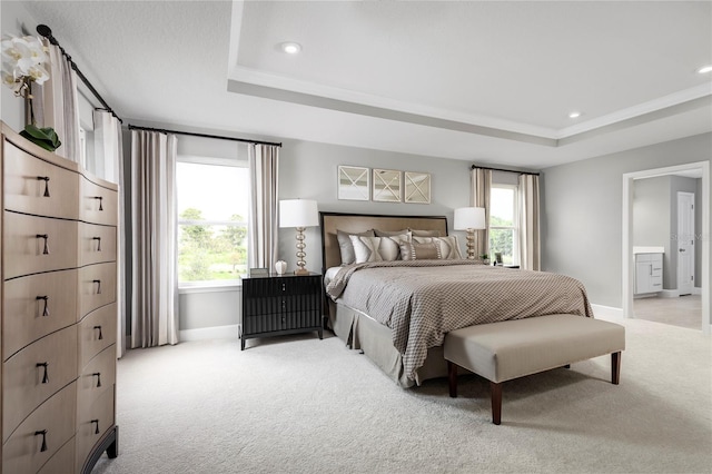 bedroom with light carpet, a tray ceiling, ensuite bath, and ornamental molding