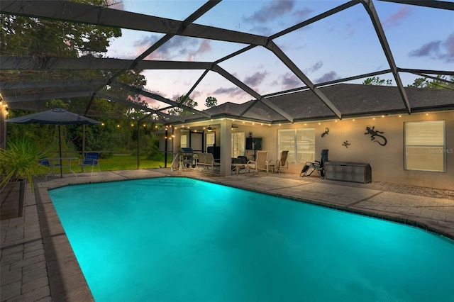 pool at dusk with ceiling fan, a patio area, and glass enclosure