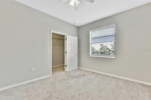 unfurnished bedroom with ceiling fan, a walk in closet, a closet, and light colored carpet