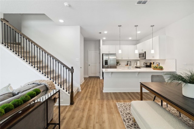 kitchen with white cabinetry, stainless steel appliances, kitchen peninsula, pendant lighting, and a breakfast bar