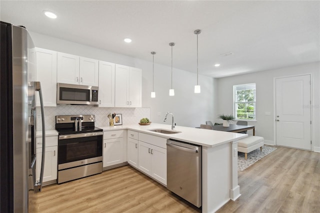 kitchen with sink, hanging light fixtures, stainless steel appliances, kitchen peninsula, and white cabinets