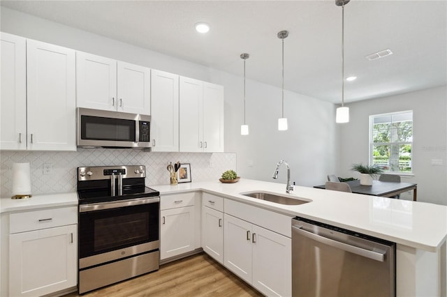 kitchen with kitchen peninsula, appliances with stainless steel finishes, sink, decorative light fixtures, and white cabinetry