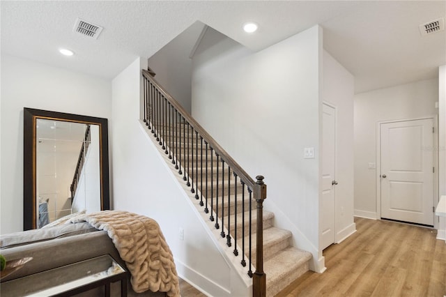 stairway with wood-type flooring and a textured ceiling